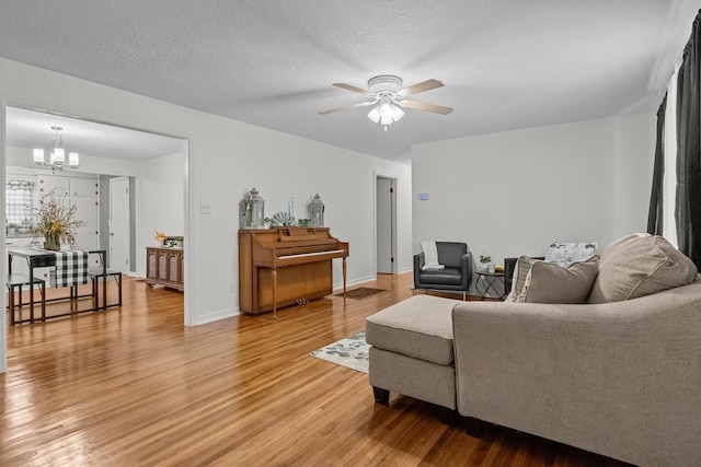 living room featuring hardwood / wood-style flooring, ceiling fan with notable chandelier, and a textured ceiling