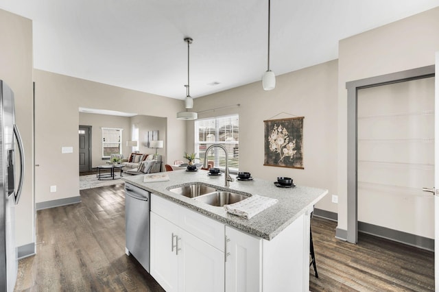 kitchen with light stone counters, stainless steel appliances, sink, white cabinetry, and hanging light fixtures