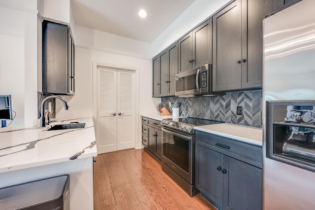 kitchen featuring backsplash, sink, light hardwood / wood-style flooring, light stone countertops, and stainless steel appliances