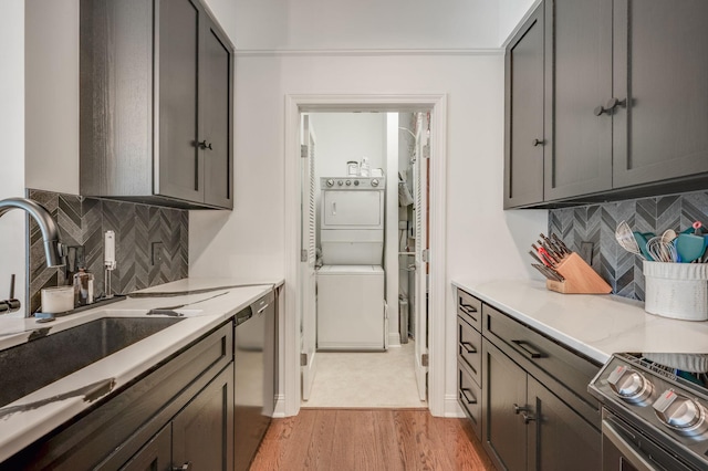 kitchen featuring sink, stainless steel appliances, light hardwood / wood-style flooring, backsplash, and stacked washer / drying machine