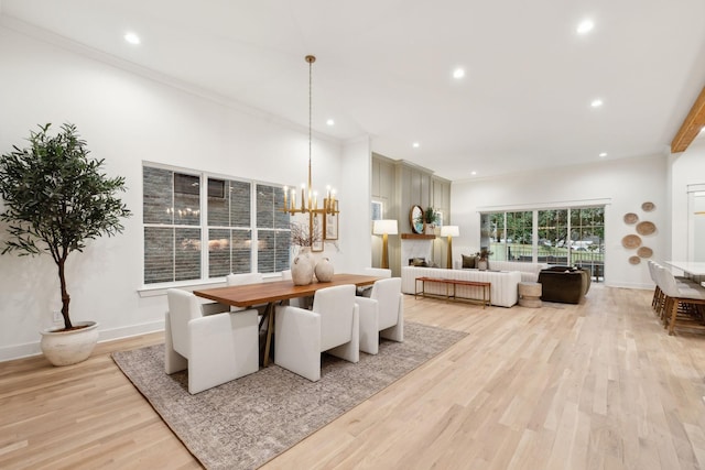 dining area featuring baseboards, a large fireplace, light wood-style floors, and an inviting chandelier