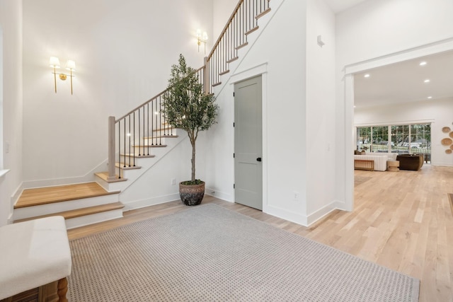 foyer with wood finished floors, recessed lighting, baseboards, a towering ceiling, and stairs