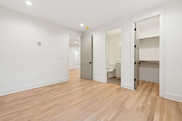 unfurnished bedroom featuring light wood finished floors, a spacious closet, baseboards, recessed lighting, and ensuite bathroom