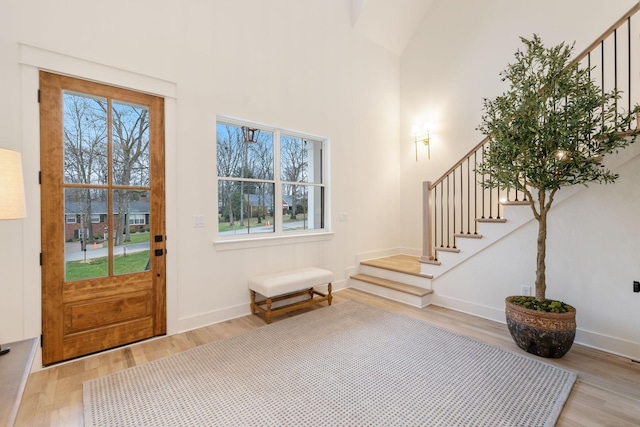 foyer featuring stairway, baseboards, light wood-style floors, and a towering ceiling