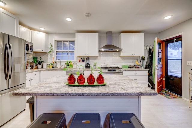 kitchen with a breakfast bar, a sink, white cabinetry, appliances with stainless steel finishes, and wall chimney range hood