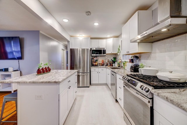 kitchen with a breakfast bar, white cabinets, wall chimney exhaust hood, appliances with stainless steel finishes, and light stone counters