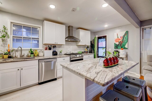 kitchen with sink, wall chimney range hood, a breakfast bar, white cabinets, and appliances with stainless steel finishes