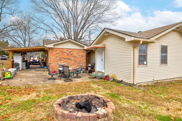 rear view of property featuring entry steps, a fire pit, a patio, a carport, and brick siding