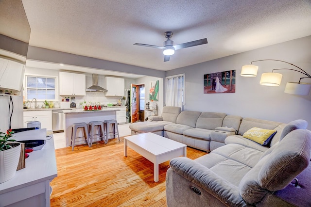 living room with ceiling fan, plenty of natural light, a textured ceiling, and light wood-type flooring