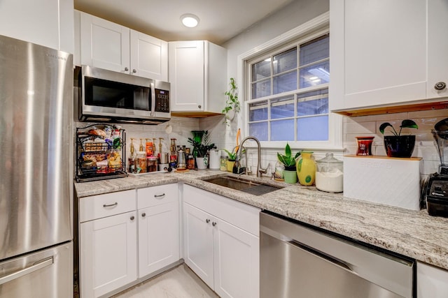 kitchen with stainless steel appliances, a sink, white cabinets, backsplash, and light stone countertops