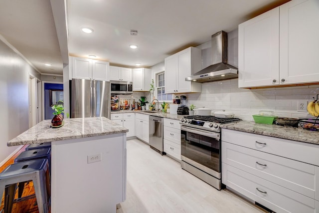 kitchen with white cabinets, wall chimney exhaust hood, a kitchen island, and stainless steel appliances