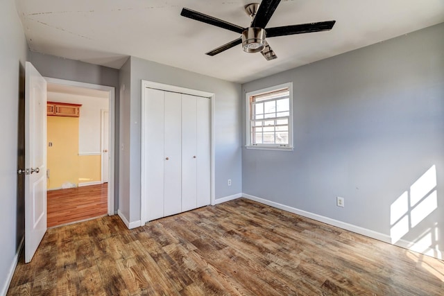 unfurnished bedroom with dark wood-type flooring, a closet, ceiling fan, and baseboards