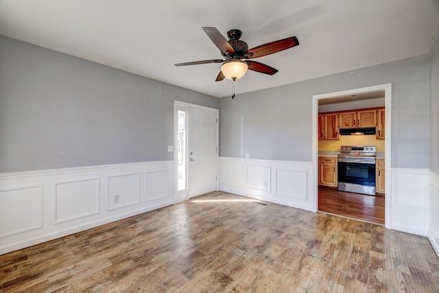 unfurnished room featuring a ceiling fan, a wainscoted wall, and light wood-style flooring