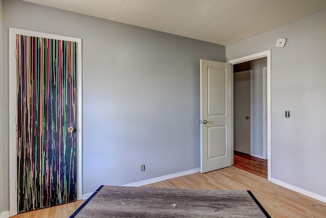 unfurnished bedroom with a textured ceiling, baseboards, and wood finished floors