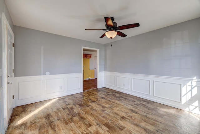 unfurnished room with a ceiling fan, a wainscoted wall, and wood finished floors