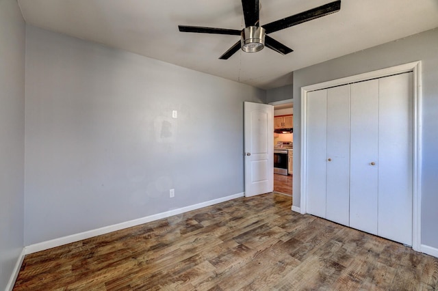 unfurnished bedroom with a closet, wood finished floors, a ceiling fan, and baseboards