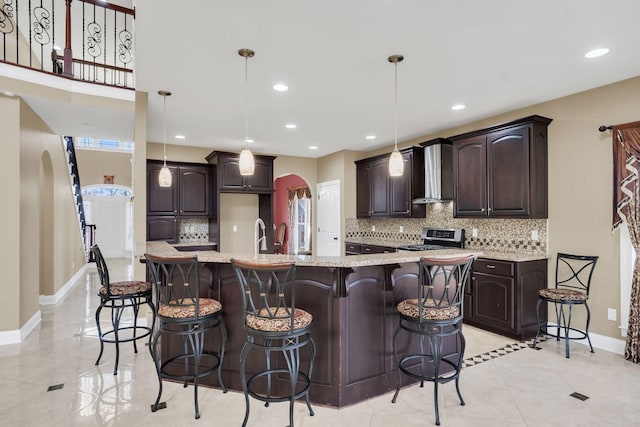 kitchen with stainless steel range, decorative light fixtures, a spacious island, and wall chimney range hood