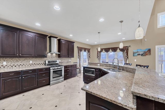 kitchen with pendant lighting, stainless steel appliances, wall chimney exhaust hood, and sink