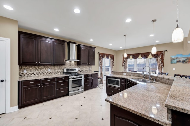 kitchen featuring wall chimney range hood, sink, appliances with stainless steel finishes, decorative light fixtures, and dark brown cabinetry