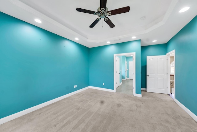 spare room with ceiling fan, a raised ceiling, and light carpet