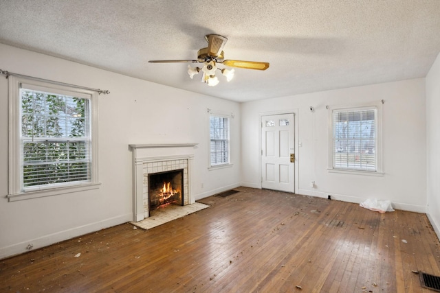 unfurnished living room with ceiling fan, a healthy amount of sunlight, wood-type flooring, and a fireplace