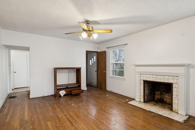 unfurnished living room featuring a tile fireplace, hardwood / wood-style floors, a textured ceiling, and ceiling fan