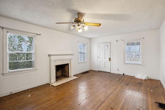 unfurnished living room featuring ceiling fan, plenty of natural light, a fireplace, and hardwood / wood-style floors