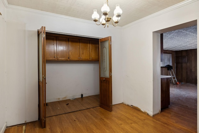 unfurnished dining area featuring crown molding, hardwood / wood-style floors, and a notable chandelier