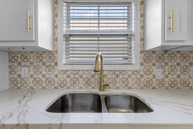 details with white cabinets, backsplash, light stone counters, and sink