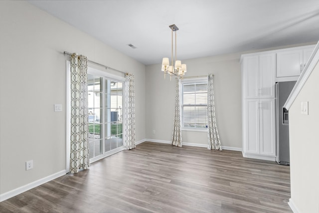 unfurnished dining area with a wealth of natural light, hardwood / wood-style flooring, and a notable chandelier