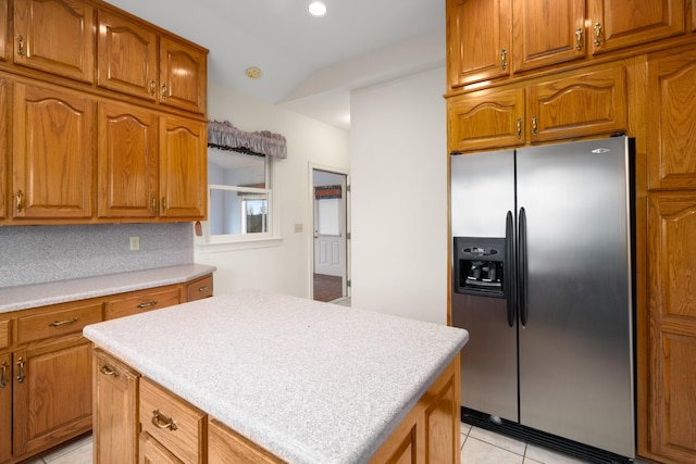 kitchen with decorative backsplash, vaulted ceiling, stainless steel fridge with ice dispenser, a kitchen island, and light tile patterned flooring