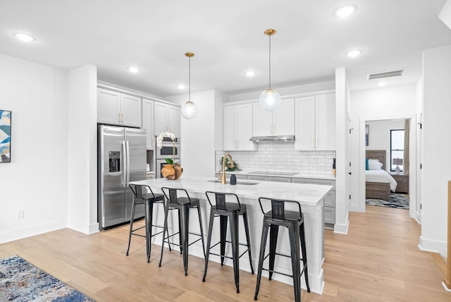 kitchen featuring white cabinets, sink, stainless steel fridge, an island with sink, and decorative light fixtures