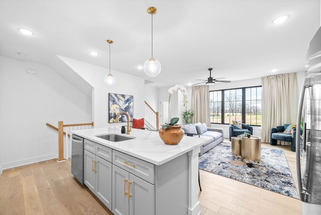 kitchen featuring ceiling fan, sink, light stone counters, decorative light fixtures, and a center island with sink