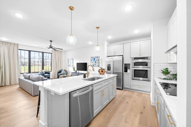 kitchen with a center island with sink, sink, hanging light fixtures, tasteful backsplash, and stainless steel appliances