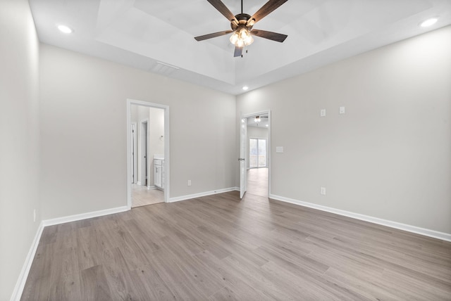 spare room with ceiling fan, light hardwood / wood-style flooring, and a tray ceiling