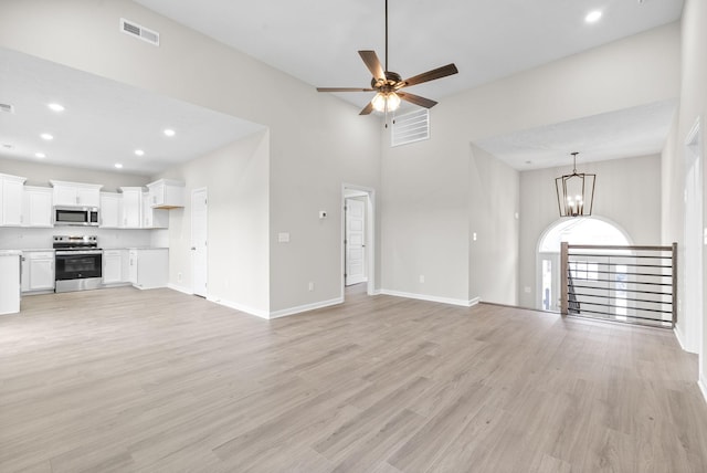 unfurnished living room featuring a high ceiling, ceiling fan with notable chandelier, and light hardwood / wood-style floors