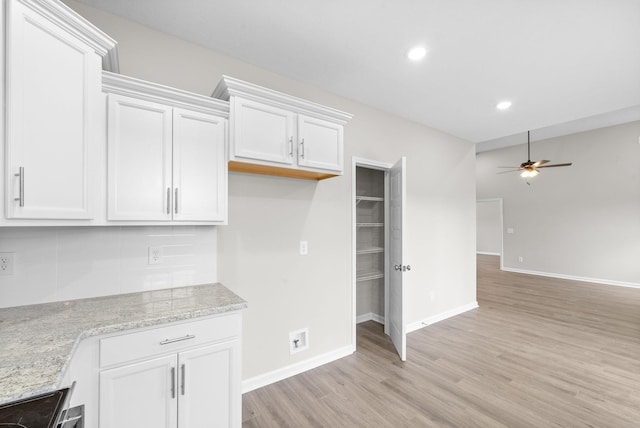 kitchen with light stone countertops, white cabinets, light hardwood / wood-style floors, and ceiling fan