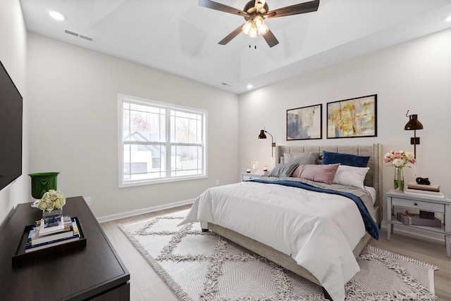 bedroom with a raised ceiling, ceiling fan, and light wood-type flooring