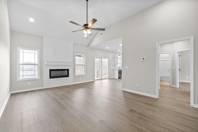 unfurnished living room with ceiling fan, a large fireplace, high vaulted ceiling, and light wood-type flooring