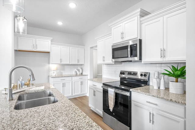 kitchen featuring appliances with stainless steel finishes, backsplash, sink, white cabinets, and hanging light fixtures