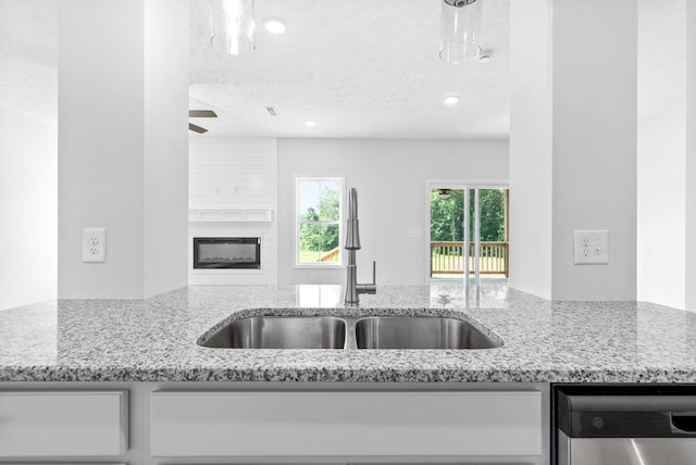 kitchen featuring a large fireplace, light stone counters, sink, and stainless steel dishwasher