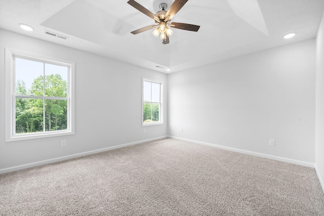 empty room with carpet flooring, ceiling fan, and a raised ceiling