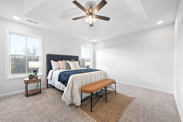 carpeted bedroom with ceiling fan and a raised ceiling