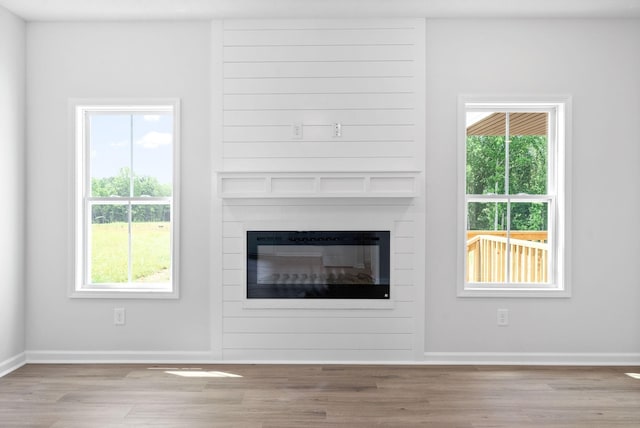 unfurnished living room featuring light wood-type flooring, a large fireplace, and a healthy amount of sunlight