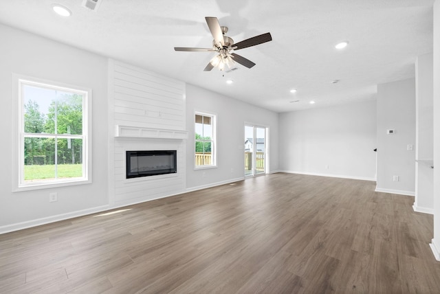 unfurnished living room with hardwood / wood-style floors, ceiling fan, and a large fireplace