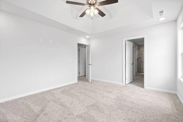 unfurnished bedroom featuring ceiling fan, light carpet, connected bathroom, and a tray ceiling