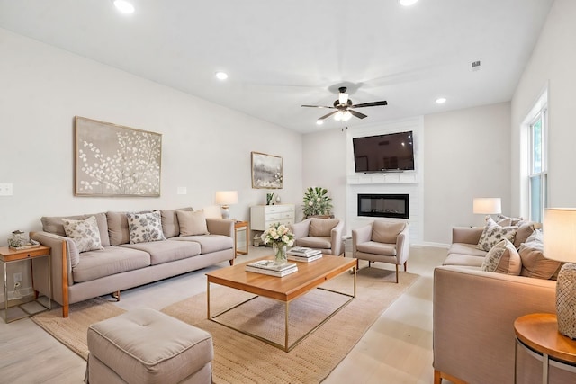 living room featuring ceiling fan, a large fireplace, and light hardwood / wood-style flooring