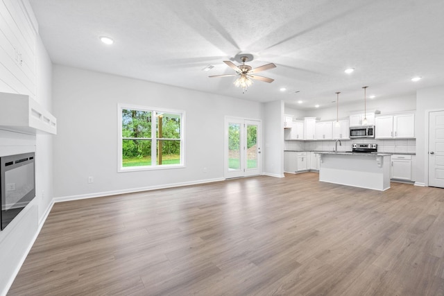 unfurnished living room with a textured ceiling, light wood-type flooring, ceiling fan, and sink