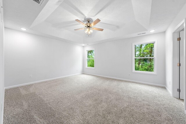 carpeted empty room with a raised ceiling and ceiling fan