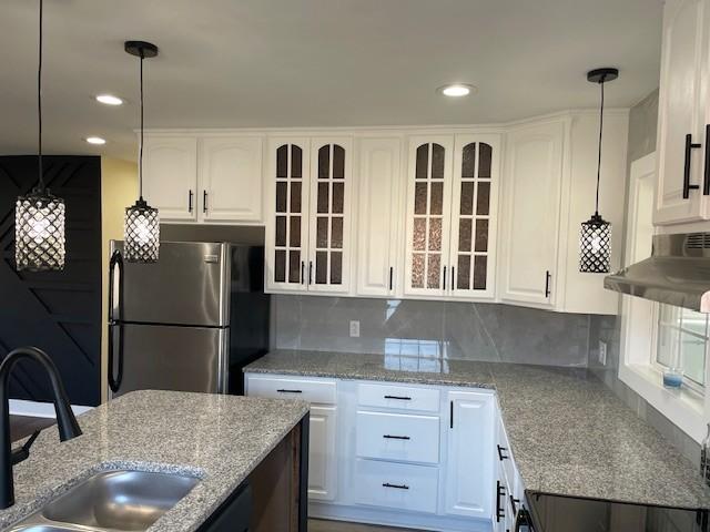 kitchen with white cabinetry, sink, stainless steel fridge, and hanging light fixtures